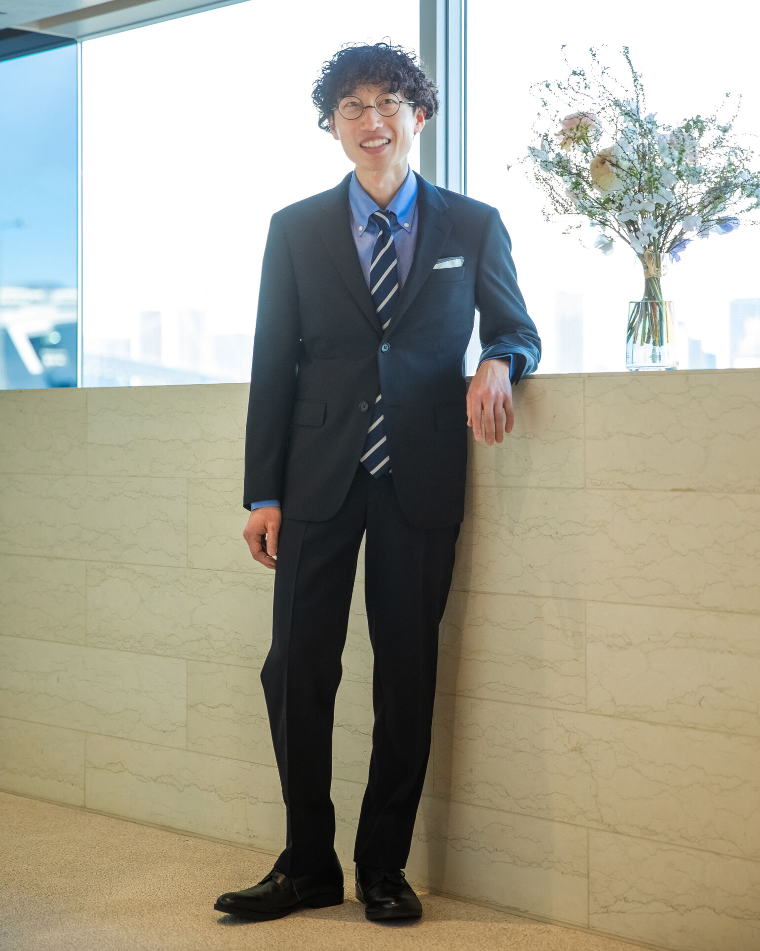 肘を掛けながらこちらを見つめるスーツを着たYoshihikoさんの画像