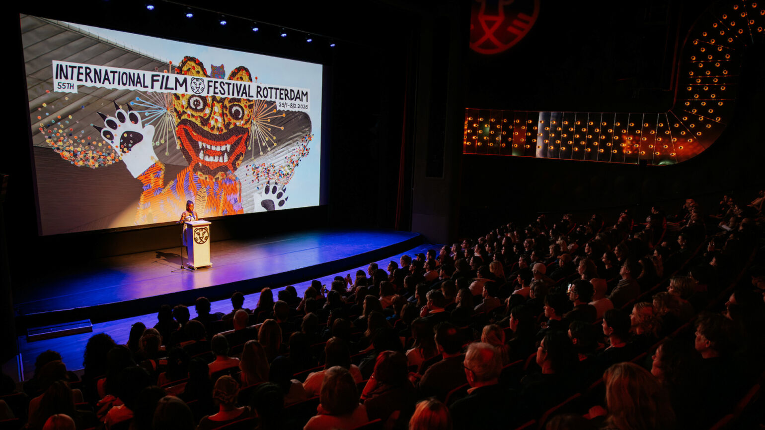 大きなスクリーンに映し出された国際映画祭のロゴを背景に、壇上の人物がスピーチをしている画像。