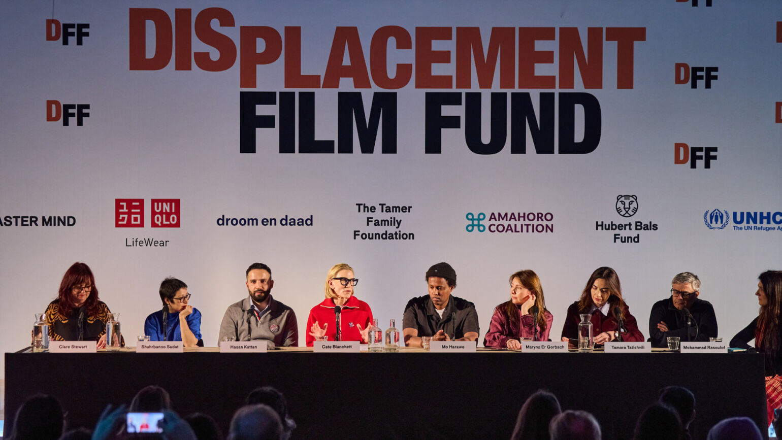 記者会見の席で、ケイト・ブランシェットさんを含む関係者たちが横一列に座り、マイクを通して話している画像。