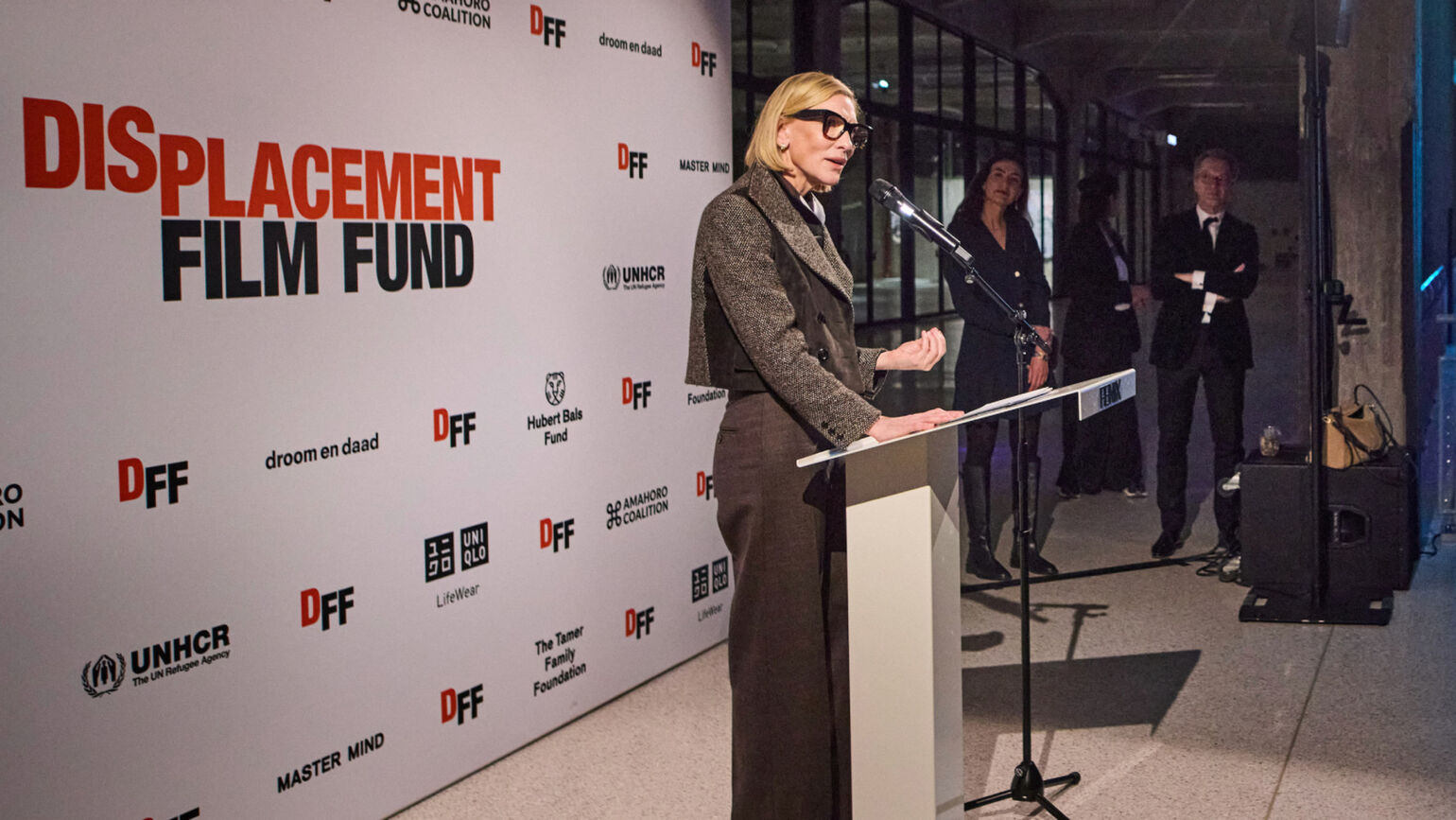 ケイト・ブランシェットさんが演台に立ち、背景に活動ロゴが並ぶステージでスピーチをしている画像。