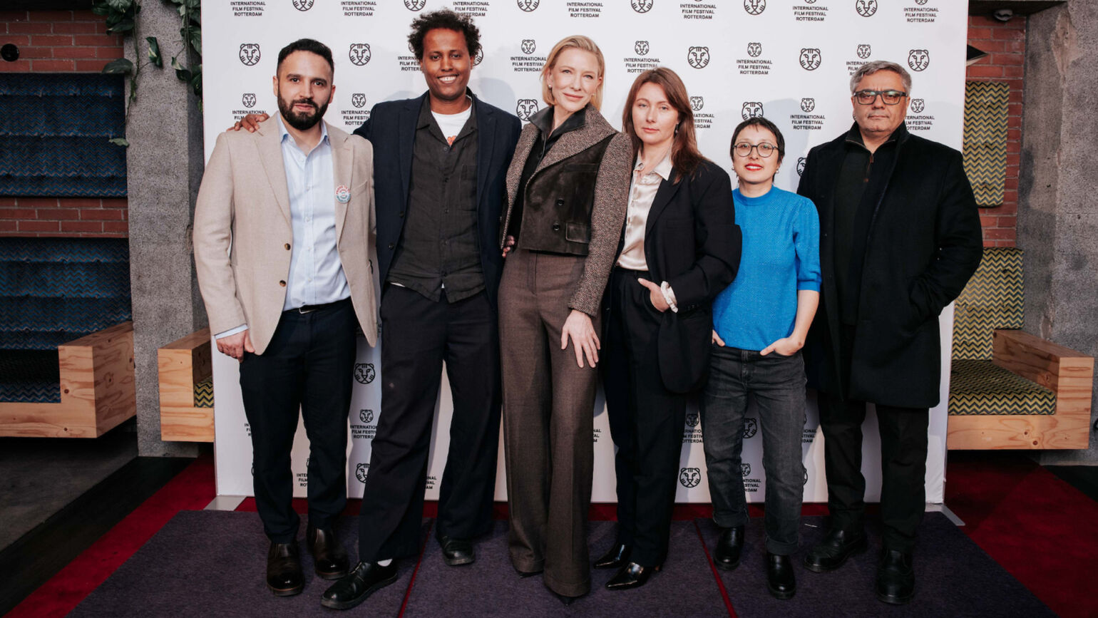 ケイト・ブランシェットさんを含む関係者たちが、ロゴの並ぶバックボードの前で肩を並べている画像。