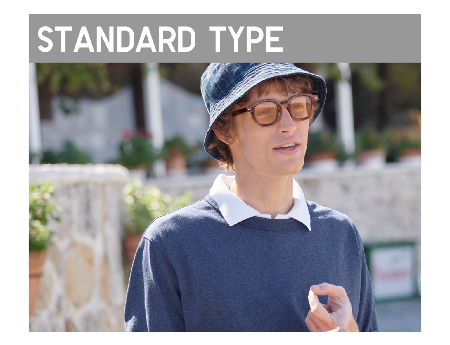 「STANDARD TYPE」のグレーのバナーの下で、茶系のレンズのサングラスとチェック柄のハット、ネイビーのカットソーを身に纏った男性が屋外で話している画像。